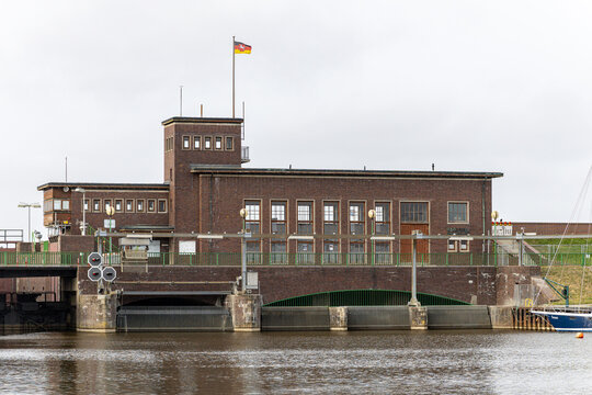 View of the Schleuse Harlesiel brick building and canal under an overcast sky in Wittmund, Niedersachsen, Germany.