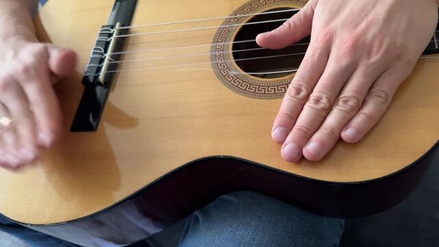 Person hitting acoustic guitar body with palm close up at home, producing strong rhythmic percussion sound, improvised music activity, creative hobby concept
