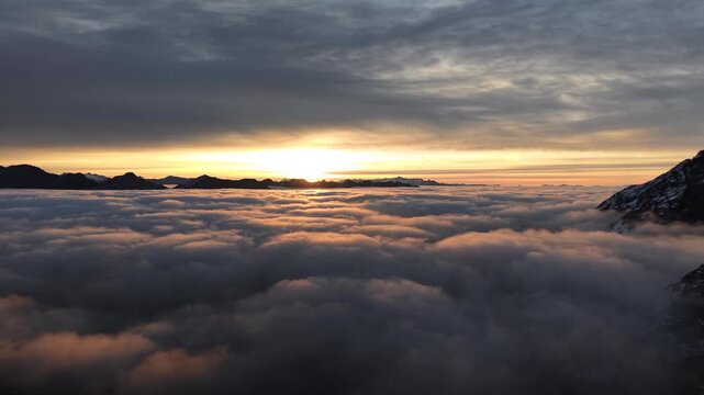 Aerial flyover over hikers enjoying the sunrise glow over the inversion of clouds in the Swiss Alps with a panoramic pan down view of the mountains and colorful sky