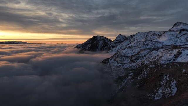 Aerial flyover over a inversion of clouds glowing at sunrise in the Swiss Alps with a panoramic view of the mountains and colorful sky