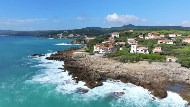 gorgeous aerial spinning reveal of private homes off a rocky beach with whitecap waves offshore in Castiglioncello, Italy
