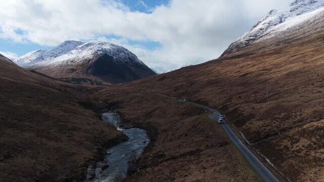 Aerial view of cars driving on a winding road next to the river etive, flowing through the scenic valley of glen coe in scotland