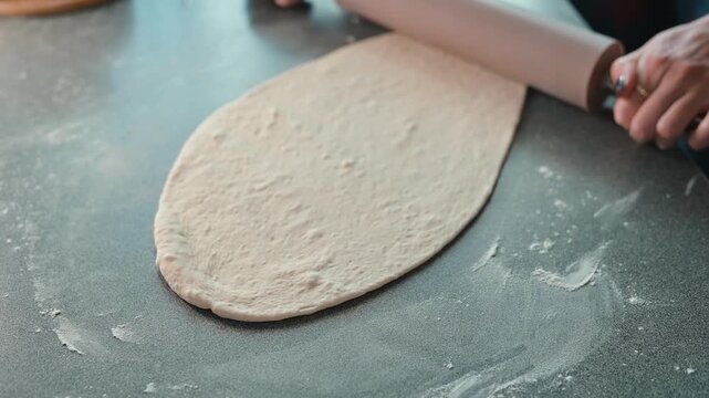 A person rolls out dough on a flat surface using a rolling pin. The kitchen is well-lit, and the focus is on the technique of flattening the dough for various baking projects