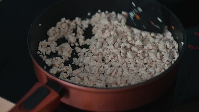 Ground meat is being cooked in a pan over medium heat, with a spatula stirring to break it apart.