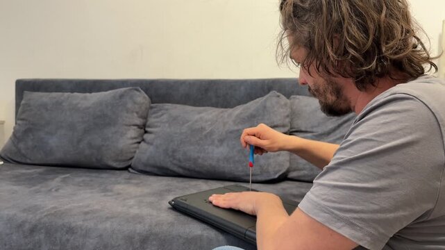 Man unscrewing laptop case with screwdriver, opening device for repair or maintenance, home electronics service concept