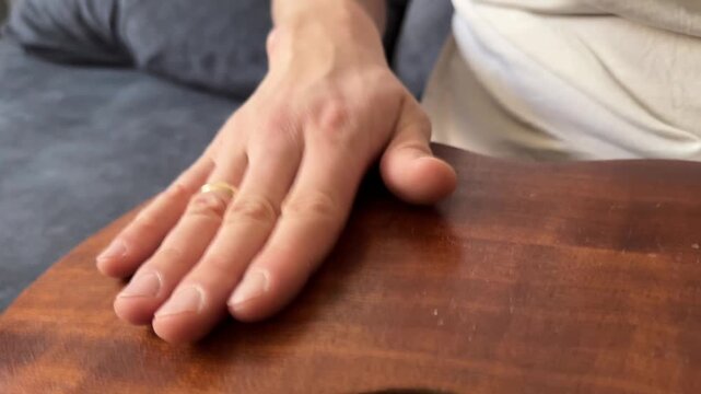 Person hitting acoustic guitar body with palm close up at home, producing strong rhythmic percussion sound, improvised music activity, creative hobby concept