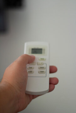 Vertical defocused photo close up with selective focus. Male hand holds white air conditioner remote control, presses climate change button. Man regulates temperature at home. Real estate, rent house