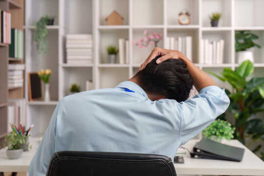 Asian man stretching neck to relieve pain during work at office desk