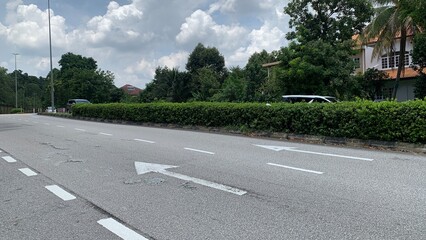 Obraz premium Empty road surface with painted directional arrows surrounded by trees and residential buildings