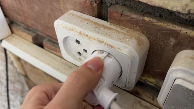 Hand plugging electrical cord into wall socket, home power connection concept, everyday electricity and appliance use