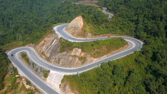 Aerial view of winding mountain road in Ha Giang, Vietnam. Sharp curves, lush green forest, and dramatic terrain create stunning aerial view of scenic Asian landscapes and travel routes.