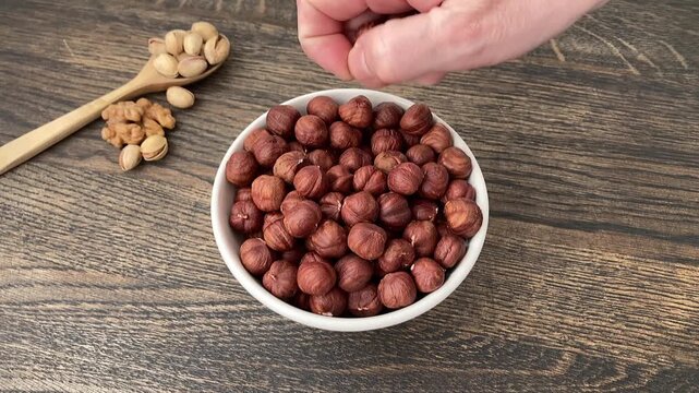 A woman takes a hazelnut from a plate. A woman's hand with hazelnuts. A light and healthy snack based on plant products. Vegetarianism. Nutritious food without animal products