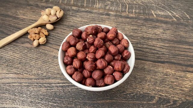 The woman adds hazelnuts to the plate. A white bowl full of nuts. Vegetarianism. A simple snack without animal products. Informed food choices and an eco-friendly lifestyle