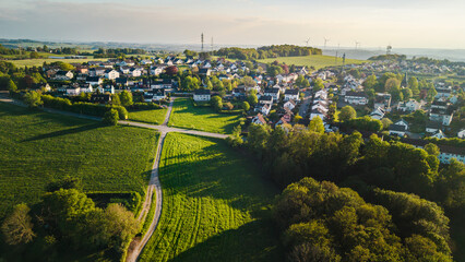 Obraz premium Aerial panorama of peaceful small town in western Germany with green farmland and residential houses during golden sunset hour
