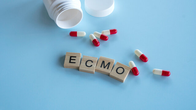 Ecmo text on wooden tiles with pharmaceutical medicine capsules and a white plastic container on a light blue background