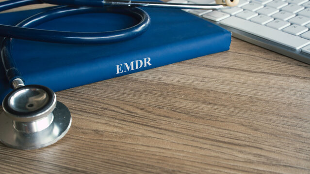 EMDR therapy concept with medical stethoscope on a blue textbook next to a computer keyboard for online mental health treatment.