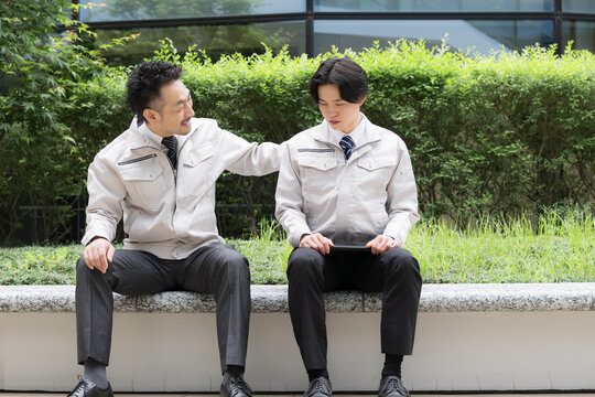 休憩中に会話する作業員のポートレート職場の人間関係性、上司が励ます落ち込む悩む部下、信頼イメージ全身　5月病の部下の話を聞く上司