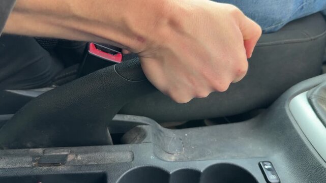 Hand releasing car handbrake lever in center console, parking brake control and driving concept