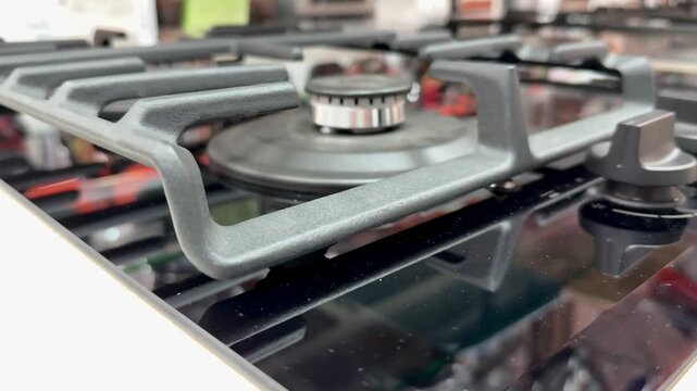 Close-up stainless gas stove knobs, top view of burners and grates, polished metal finish with subtle reflections, three circular