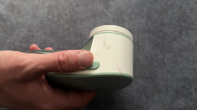 Close up hands holding fabric lint remover device, household clothing care tool and garment maintenance concept