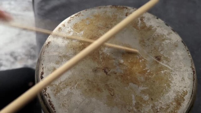 Person hitting metal pot with wooden sticks close up, creating rhythm like drum, improvised percussion activity, creative hobby concept