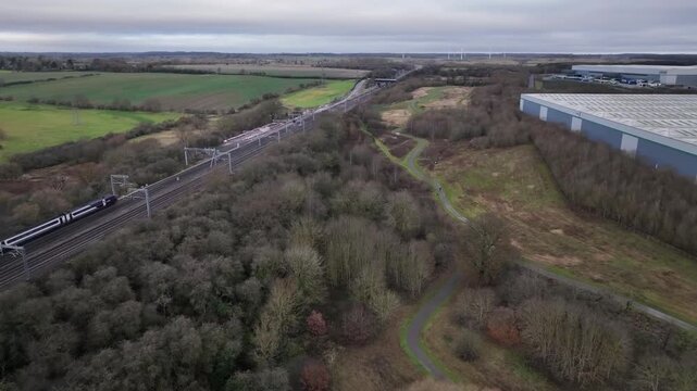 Aerial Drone View of Train Passing Through Northamptonshire Countryside Near Industrial Park