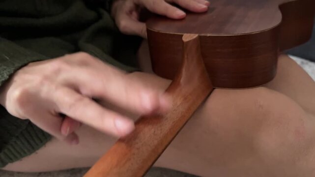 Person tapping fingers rhythmically on ukulele neck close up at home, producing soft percussion sound, improvised music activity, creative hobby concept