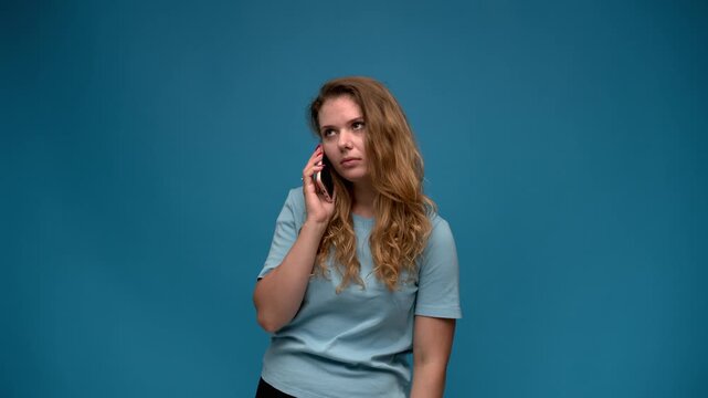 Frustrated woman experiencing mood swings while talking on the phone over a blue background