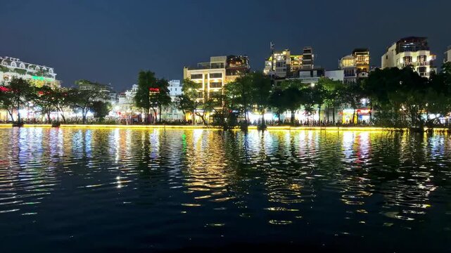Night cityscape view of Hanoi Hoan Kiem lake with vibrant building lights reflecting on dark water surface, urban atmosphere, travel destination