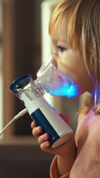 A young patient holds a nebulizer beside her crib, receiving inhalation therapy for respiratory problems such as bronchitis and pneumonia, loosening sputum and easing breathing difficulties