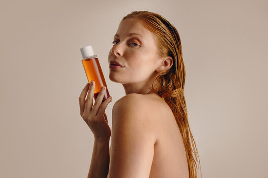 Redhead woman holding amber skincare bottle in profile
