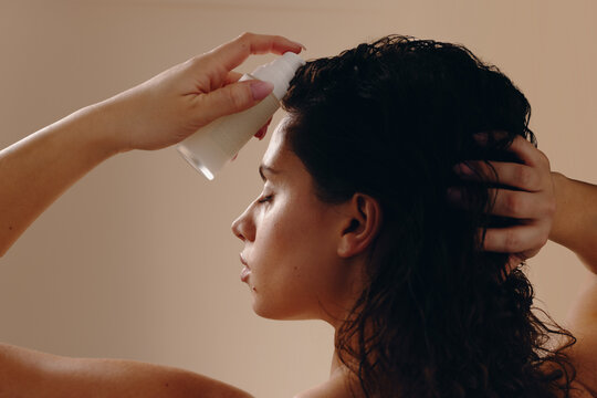 Woman applying hair serum to wet hair with hand holding bottle