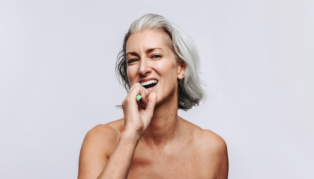 Mature woman laughing while brushing her teeth in studio