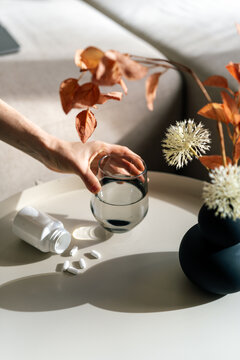 Woman takes medication while sitting in a living room by a table with water