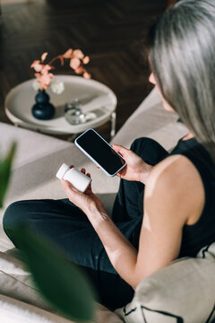 Woman takes prescription pill while checking phone in living room
