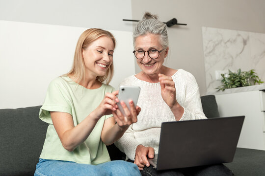 Young adult woman showing smartphone to senior woman at home