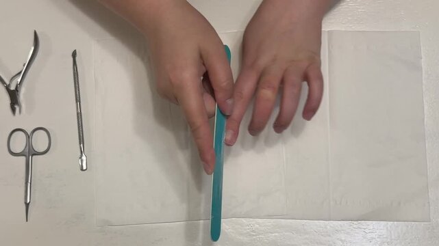 A woman files her nails with a blue nail file against a white background; a concept for a home manicure and hand care