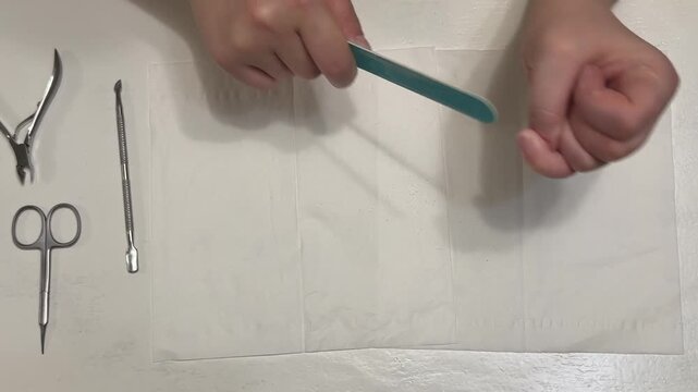 A woman files her nails with a blue nail file against a white background; a concept for a home manicure and hand care