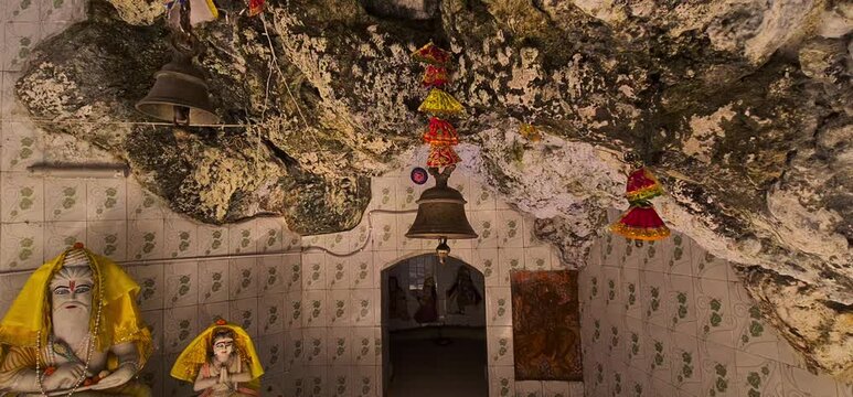 Hindu temple interior with statues and hanging bells inside cave shrine, Dehradun, India 