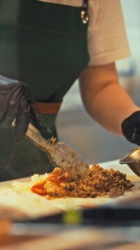 In a lively fast-food restaurant kitchen, a chef deftly fills pita breads with seasoned meat and crisp vegetables, the air buzzing with sizzling aromas as lunchtime service ramps up
