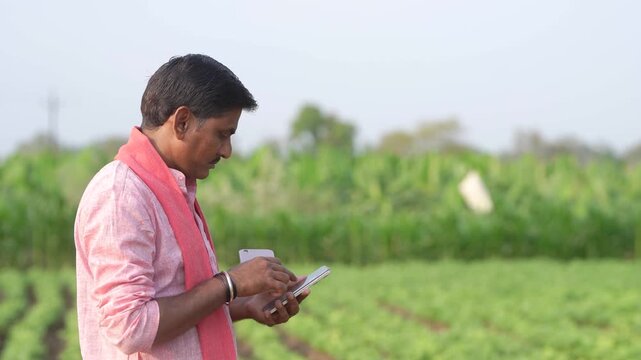 young indian farmer using smartphone sitting at green agricultural field