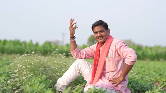 happy young indian farmer sitting at green agricultural field