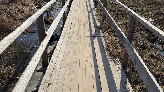 Temporary wooden bridge over dry grass, narrow plank walkway with handrails casting long shadows across dead brown vegetation