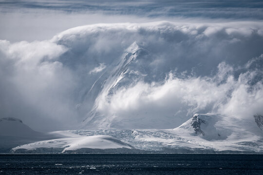 View of snow-covered mountain peaks partially obscured by thick white clouds above the dark blue sea Antarctica.