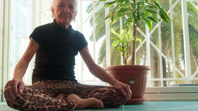 senior lady woman meditate cross legs buddhist mantra in bright terrace nearby a plant , concept of wellbeing aging prayer