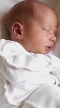 A sleeping baby rests peacefully on a soft surface. The baby is wrapped in a cozy, light-colored outfit, embodying tranquility and innocence.