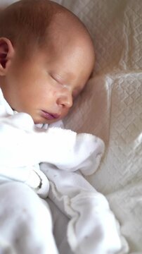 A sleeping baby is nestled comfortably on a soft surface. The tranquil baby is wrapped in white fabric, showcasing peaceful features in the gentle light.