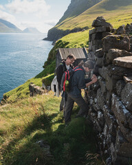 Two hikers searching for a geocache in a stone wall along the dramatic coastline of the Faroe Islands © hopsalka