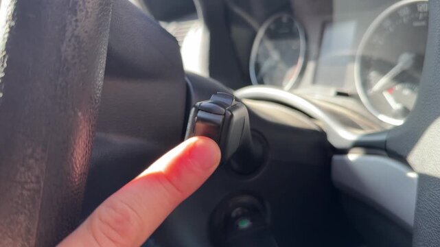 Hand operating turn signal lever behind steering wheel, car driving control and road safety concept