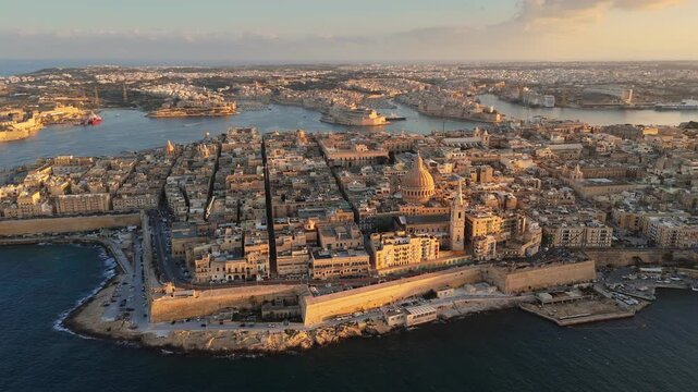 Aerial of defensive stone walls protecting coastal peninsula of Valletta, Malta. Sunset light illuminates historic buildings of Valletta, Malta. Mediterranean sea borders the harbor of Valletta
